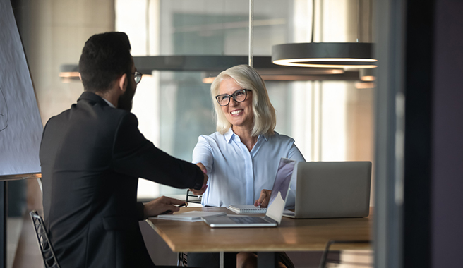 Smiling mature businesswoman shaking hand of young businessman